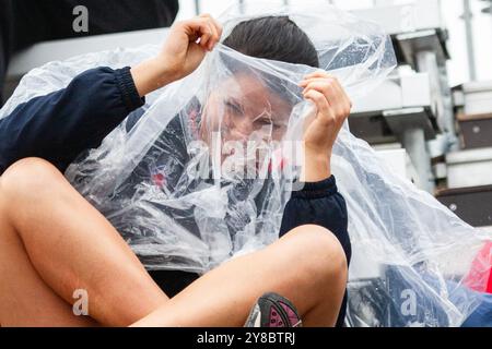 HUMOUR SOUS LA PLUIE, TEMPÊTE ESTIVALE, BEACH VOLLEY, MARIEHAMN, 2011 : une jeune femme voit le côté drôle des choses. La foule se couvre avec des ponchos jetables alors qu'une énorme tempête estivale balaye le stade avec un déluge de pluie pendant les demi-finales en août 2011 au PAF Open à Mariehamn, Åland, Finlande. Photographie : Rob Watkins. INFO : entre 2009-2013, le tournoi PAF Open Beach Volleyball était un événement annuel organisé à Mariehamn, Åland, Finlande. Il a attiré les meilleures équipes et joueurs internationaux en tant que partie du classement officiel du circuit mondial FIVB, mettant en vedette le vol de plage de haut niveau Banque D'Images