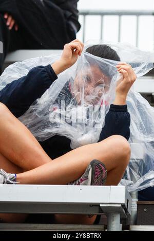 HUMOUR SOUS LA PLUIE, TEMPÊTE ESTIVALE, BEACH VOLLEY, MARIEHAMN, 2011 : une jeune femme voit le côté drôle des choses. La foule se couvre avec des ponchos jetables alors qu'une énorme tempête estivale balaye le stade avec un déluge de pluie pendant les demi-finales en août 2011 au PAF Open à Mariehamn, Åland, Finlande. Photographie : Rob Watkins. INFO : entre 2009-2013, le tournoi PAF Open Beach Volleyball était un événement annuel organisé à Mariehamn, Åland, Finlande. Il a attiré les meilleures équipes et joueurs internationaux en tant que partie du classement officiel du circuit mondial FIVB, mettant en vedette le vol de plage de haut niveau Banque D'Images