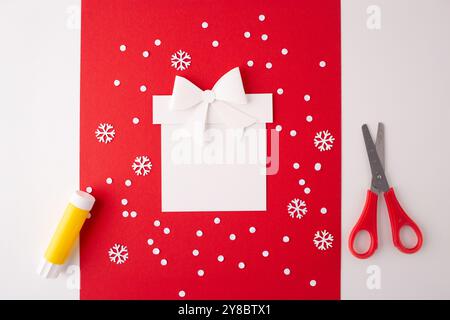 coffret cadeau blanc découpes en papier de flocons de neige, donnant l'impression de tomber de la neige. bâton de colle jaune, une paire de ciseaux fermés avec des poignées rouges. Décoration de vacances de bricolage ou projet de carte de voeux, Banque D'Images