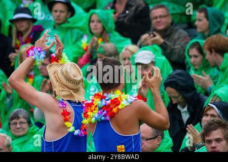 FANS DE LEIS HAWAÏENS, TEMPÊTE ESTIVALE, BEACH VOLLEY, MARIEHAMN, 2011 : deux fans de leis hawaïens essaient de remonter le moral. La foule se couvre avec des ponchos jetables alors qu'une énorme tempête estivale balaye le stade avec un déluge de pluie pendant les demi-finales en août 2011 au PAF Open à Mariehamn, Åland, Finlande. Photographie : Rob Watkins. INFO : entre 2009-2013, le tournoi PAF Open Beach Volleyball était un événement annuel organisé à Mariehamn, Åland, Finlande. Il a attiré les meilleures équipes et joueurs internationaux en tant que partie du classement du circuit mondial officiel de la FIVB, mettant en vedette le high leve Banque D'Images