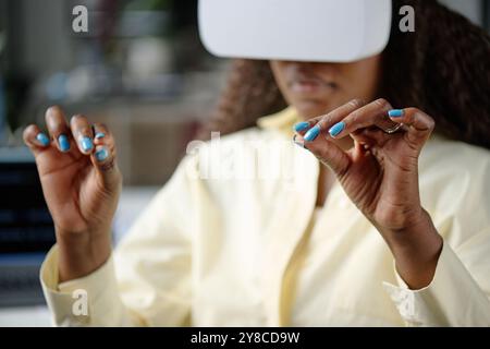 Gros plan moyen de mains féminines manucurées gesticulant dans l'air pendant que la femme joue à un jeu VR Banque D'Images