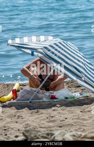 lady ombrage du soleil chaud méditerranéen d'été sous un parasol ou parasol sur une plage en saison estivale, parasol rayé Banque D'Images