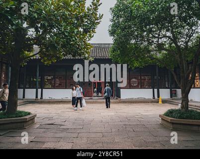 Suzhou, Chine - 08 octobre 2019 : les visiteurs explorent une cour traditionnelle entourée de verdure luxuriante dans un cadre architectural ancien Banque D'Images