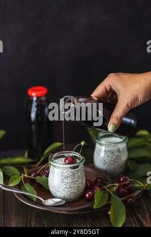 Femme versant du jus de cerise sur un parfait pudding aux graines de chia décoré de cerises fraîches Banque D'Images