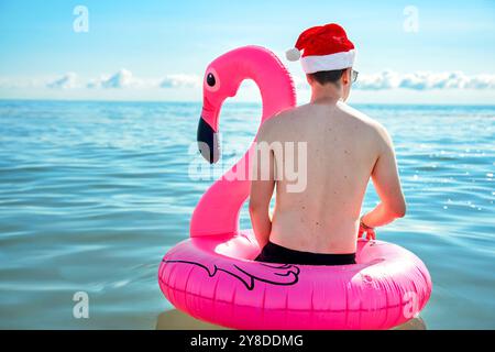 7 septembre 2024 : image symbolique pour des vacances d'hiver avec une touche estivale. Un homme dans un chapeau de Noël est assis dans un anneau rose flamant nageant dans la mer au soleil *** Symbolbild für Winterurlaub mit sommerlichem Flair. Ein Mann mit Weihnachtsmütze sitzt in einem rosa Flamingo-Schwimmring im Meer BEI Sonnenschein Banque D'Images