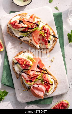 Deux tranches de pain avec des figues et du jambon sur une assiette blanche. L'assiette est sur une table avec un tissu vert Banque D'Images