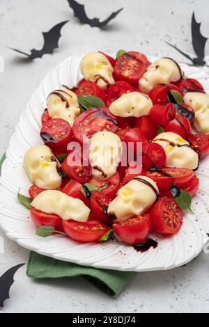 Salade Caprese avec tomates mûres, crâne de fromage mozzarella, feuilles de basilic et glaçage balsamique pour Halloween Banque D'Images