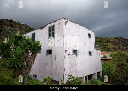 Maison blanche altérée entourée de verdure luxuriante sous un ciel orageux dans un village à flanc de colline Banque D'Images