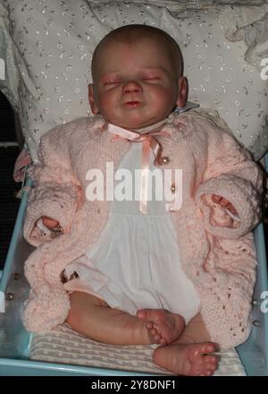 Poupée bébé mignon renaissance dormant dans le lit sur un grand oreiller blanc, endormi rétro jouet vintage portant des vêtements roses Banque D'Images