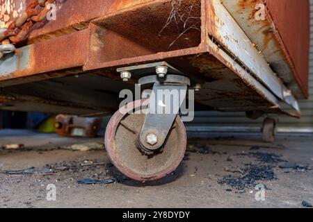 Photographie d'une roulette vieille et sale sur une grande poubelle en acier rouillé à l'extérieur d'une usine de fabrication industrielle. Banque D'Images