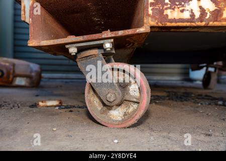 Photographie d'une roulette vieille et sale sur une grande poubelle en acier rouillé à l'extérieur d'une usine de fabrication industrielle. Banque D'Images