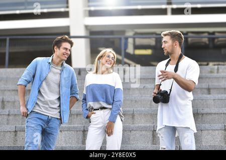 Trois amis heureux de parler en tenant une conversation dans la rue dans une journée ensoleillée avec des bâtiments en arrière-plan Banque D'Images