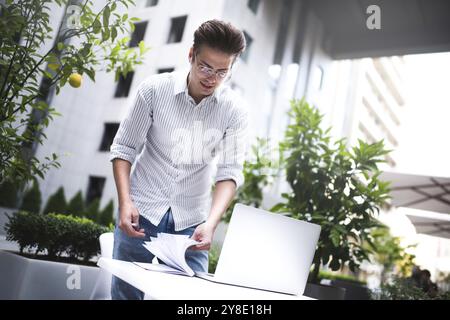 Heureux homme d'affaires beau mélange sa pause et son travail à l'extérieur, homme d'affaires avec des écouteurs écrire quelques nouvelles idées dans le cahier assis dans le café Banque D'Images