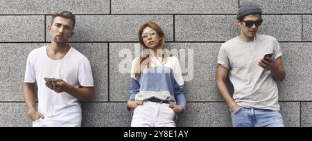 Portrait de mode de trois meilleurs amis posant dans la rue, portant une tenue élégante et un Jean contre le mur gris Banque D'Images