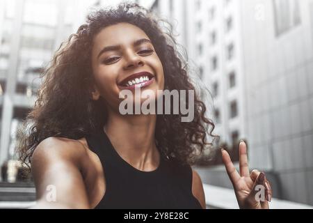 Portrait en plein air belle femme afroamerican heureuse prenant selfie photo souriant rire avec des dents parfaites dans la rue Banque D'Images