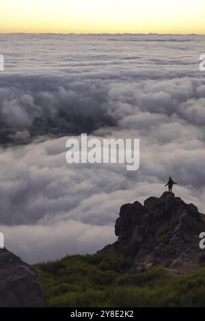 Un randonneur solitaire se tient sur un pic rocheux au-dessus d'une couverture nuageuse au coucher du soleil Banque D'Images