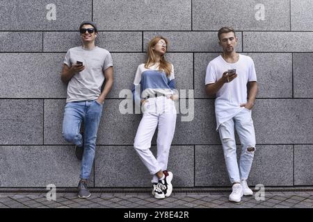 Portrait de mode de trois meilleurs amis posant dans la rue, portant une tenue élégante et un Jean contre le mur gris Banque D'Images