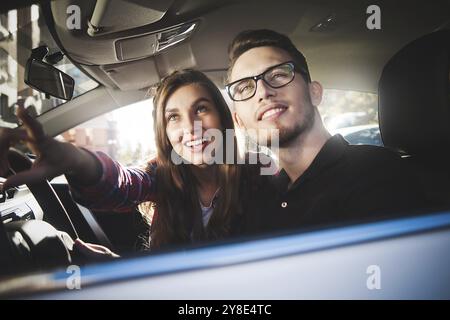 Voyager. Beau jeune couple assis sur les sièges de passager avant et souriant tout en beau homme conduisant une voiture Banque D'Images