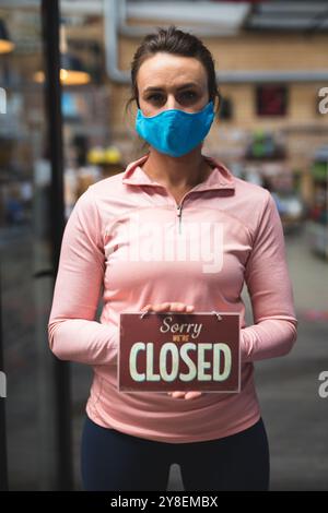 Portrait d'une femme caucasienne portant un masque tenant un signe ouvert dans le couloir au gymnase Banque D'Images