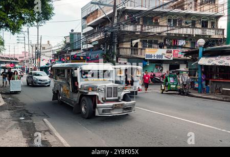 Manille, Philippines - 26 août 2019 : un jeepney dynamique conduit le long d'une rue animée remplie de boutiques et de piétons. Banque D'Images