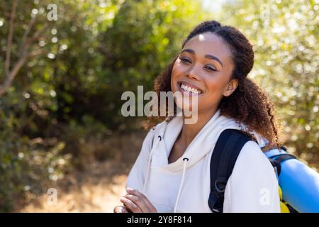 Portrait de femme biraciale heureuse regardant la caméra et souriant dans la forêt Banque D'Images