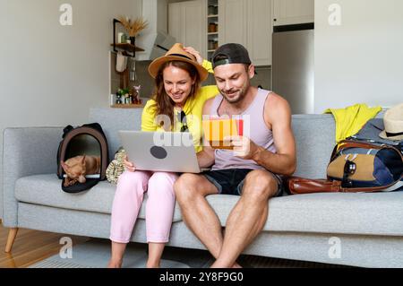 Couple avec petit chien dans le transporteur à la maison finalisant les plans de voyage avant le départ, en vérifiant les données de réservation. Banque D'Images