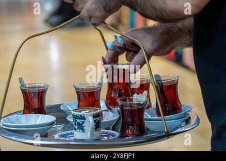 Turkiye. Istanbul. Un vendeur de thé porte un plateau rempli de verres de thé turc traditionnel, servi dans des verres à tulipes, accompagné d'une petite tasse Banque D'Images