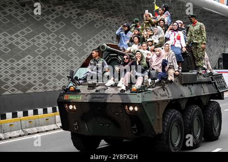 Jakarta, Indonésie. 5 octobre 2024. Des gens montent dans la rue avec des soldats des Forces armées nationales indonésiennes (TNI) à bord d’un véhicule militaire après le défilé militaire du 79e anniversaire de la TNI à Jakarta, Indonésie, le 5 octobre 2024. Crédit : Agung Kuncahya B./Xinhua/Alamy Live News Banque D'Images