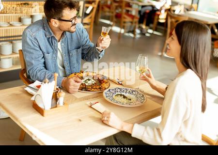 Deux personnes savourent leurs boissons à une table en bois, immergées dans une ambiance de restaurant détendue, tout en étant profondément dans la conversation et les rires. Banque D'Images