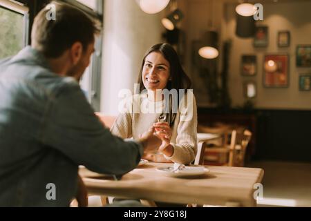 Un couple profite d'un moment agréable dans un café chaleureux, partageant des rires et de délicieuses friandises tout en se prélassant dans l'ambiance chaleureuse remplie de lumière naturelle Banque D'Images