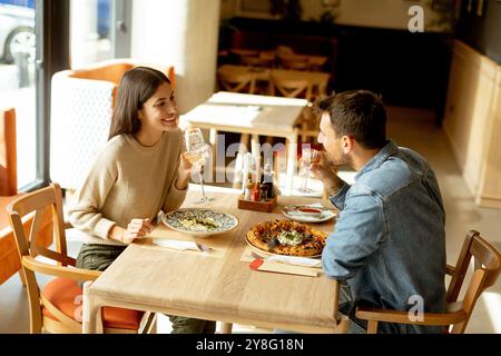 Deux personnes savourent leurs boissons à une table en bois, immergées dans une ambiance de restaurant détendue, tout en étant profondément dans la conversation et les rires. Banque D'Images