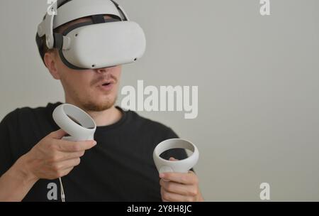 Un jeune homme jouant en utilisant des lunettes de réalité visuelle avec des joysticks avec Copy Space. Lunettes de casque VR connectant Metaverse. Futuriste Cyberspace Techno Banque D'Images
