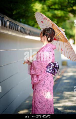 Une femme dans un kimono rose tient un parapluie traditionnel japonais marchant dans la rue. Kyoto, Japon. Banque D'Images