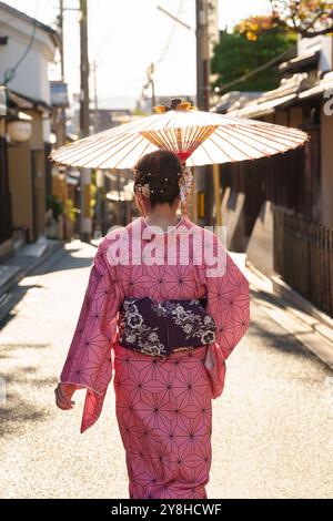 Une femme dans un kimono rose tient un parapluie traditionnel japonais marchant dans la rue. Kyoto, Japon. Banque D'Images