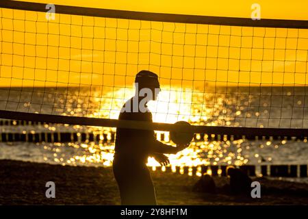 05 octobre 2024, Meckenburg-Poméranie occidentale, Graal-Müritz : un homme se tient debout avec une balle derrière un filet de volley-ball sur la plage de la mer Baltique au coucher du soleil. Les températures atteignent jusqu'à 15 degrés Celsius le dimanche. Il reste ensoleillé et sec. La probabilité de précipitations n'augmente que dans la semaine à venir. Photo : Frank Hammerschmidt/dpa Banque D'Images