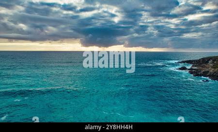 Une vue imprenable sur l'océan sous un ciel dramatique. L'eau est un turquoise vibrant, contrastant avec les nuages sombres ci-dessus. Les vagues écrasent doucement l'ag Banque D'Images