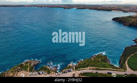 Une vue panoramique sur la côte avec un vaste océan bleu rencontrant le rivage. Le paysage comprend des falaises rocheuses et une zone herbeuse, avec un parking vis Banque D'Images