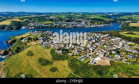 Vue aérienne d'un village côtier pittoresque entouré de collines verdoyantes et d'une baie sereine remplie de bateaux. Le village dispose de charmantes maisons A. Banque D'Images