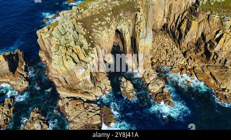 Vue aérienne des falaises côtières escarpées avec une arche rocheuse naturelle, entourée par les eaux bleu profond de l'océan. Les vagues s'écrasent contre le rivage rocheux, créant Banque D'Images