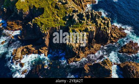 Vue aérienne des falaises côtières escarpées entourées de vagues bleu profond de l'océan. Les formations rocheuses sont recouvertes de végétation verte, créant une saisissante Banque D'Images