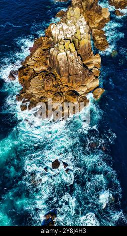 Vue aérienne des rochers côtiers accidentés entourés de vagues turquoises. L'eau s'écrase contre les formations rocheuses, créant de la mousse blanche. Le scen Banque D'Images