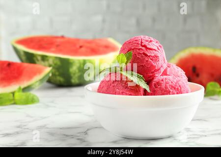 Boules de savoureux sorbet à la pastèque avec de la menthe dans un bol sur une table en marbre blanc, gros plan. Espace pour le texte Banque D'Images