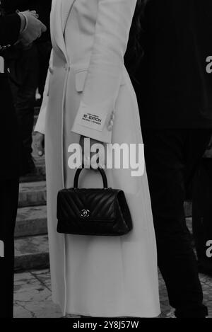 Une invitée portant un long manteau blanc classique et un petit sac à main pochette en noir de Chanel au salon Elie Saab pour Paris Fashion week SS25 Banque D'Images