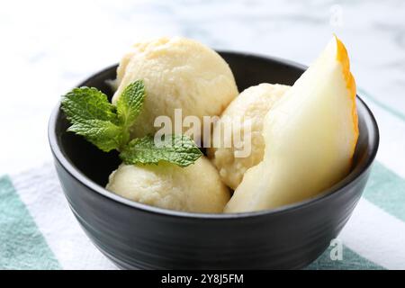 Boules de savoureux sorbet de melon avec de la menthe et des fruits frais dans un bol sur une table blanche, gros plan Banque D'Images