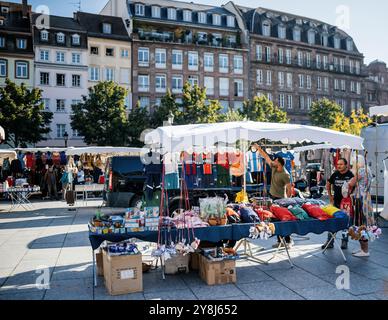 Strasbourg, France - 20 septembre 2024 : homme vendant plusieurs vêtements sur la place Kleber, Strasbourg, avec des bâtiments haussmanniens en arrière-plan, en attente de clients Banque D'Images