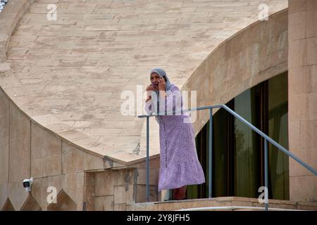 Boukhara, Ouzbékistan ; septembre,19,2024:une femme portant un hijab violet et une tenue assortie, debout sur un escalier à Boukhara, Ouzbékistan, alors que spea Banque D'Images