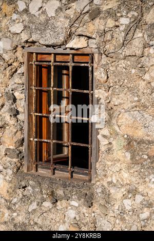 Un vieux mur de maison en pierre avec une petite fenêtre dans la lumière chaude du matin. Banque D'Images