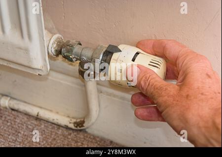 Gros plan sur les hommes plus âgés ajustant le thermostat de chauffage à la main sur le radiateur pour économiser l'énergie dans la maison Banque D'Images