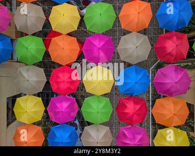 Affichage suspendu vibrant de parapluies multicolores suspendus entre deux bâtiments dans une cour urbaine étroite à Łódź, Pologne Banque D'Images
