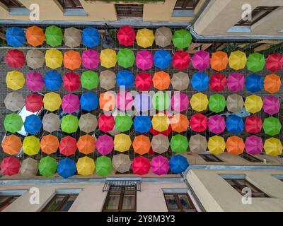 Affichage suspendu vibrant de parapluies multicolores suspendus entre deux bâtiments dans une cour urbaine étroite à Łódź, Pologne Banque D'Images